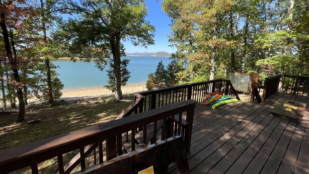 A wooden deck with a railing, overlooking a lake and beach. - Dog Friendly Lakefront Cabin with Amazing Sunset Views & New Boat dock.  (Jefferson City)