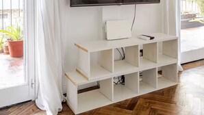 Ein Wohnzimmer mit einem an der Wand befestigten Flachbildfernseher, einer weißen Unterhaltungseinrichtung darunter und einem Holzboden mit Zinkeneinlage.