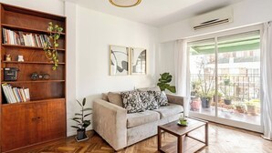 Ein Wohnzimmer mit einer Couch, einem Holzregal, einem Couchtisch und einem großen Fenster mit Blick nach draußen.