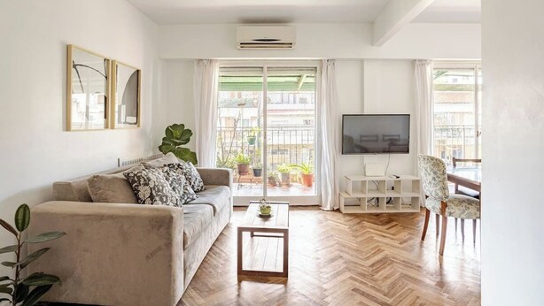 Ein Wohnzimmer mit Sofa, Couchtisch, Fernseher und einem Balkon mit Topfpflanzen.