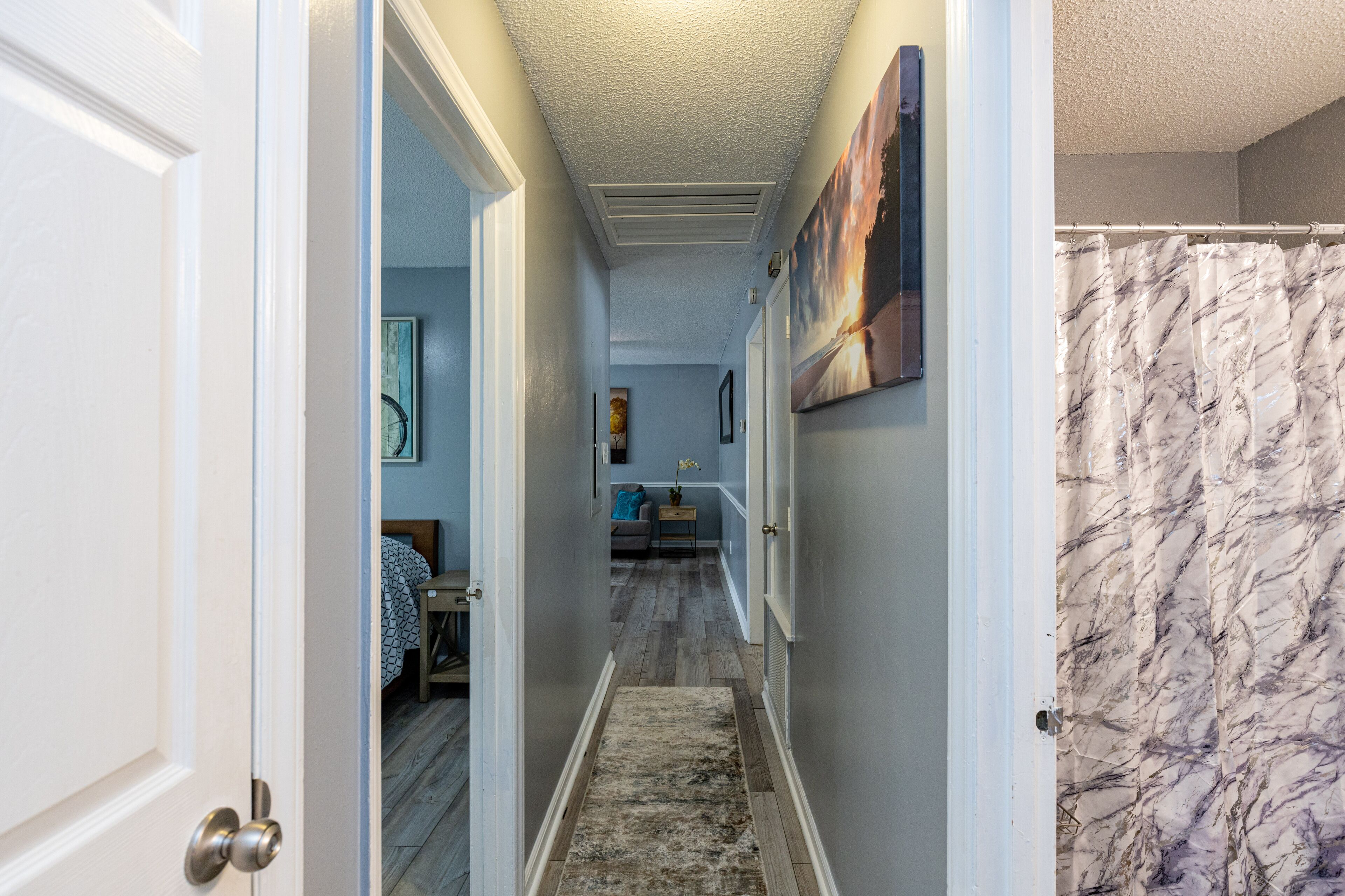 Un couloir doté d’un plancher en bois, d’un tapis et d’un rideau de douche en marbre.