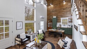A spacious living room with a large window, a wooden ceiling, a dining area, and a kitchen with green cabinets. - Couples Tree Loft  Rock Hot Tub Buffalo River (St Joe)