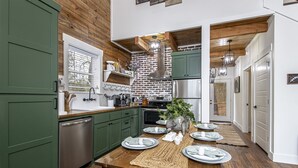 A modern kitchen with green cabinets, a wooden dining table set for four, and a brick wall backsplash. - Couples Tree Loft  Rock Hot Tub Buffalo River (St Joe)
