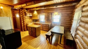 A log cabin interior with a wooden floor, a kitchen area including a sink and cabinets, and a dining table. - Clean Log Cabin in Trout Fishing mecca!!!! (Genoa)