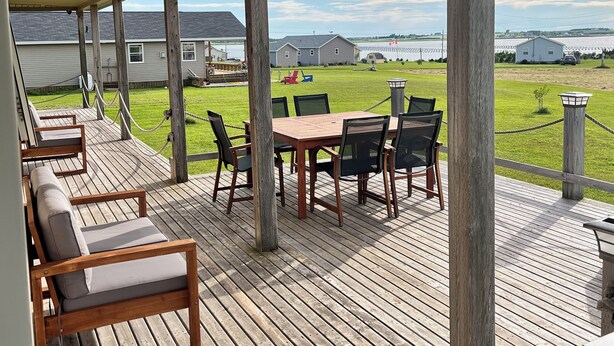 Une terrasse extérieure couverte, aménagée avec du mobilier en bois, offrant une vue sur une zone verdoyante et des bâtiments en arrière-plan.