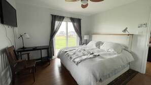 Une chambre à coucher comprenant un lit, un bureau, une chaise, un téléviseur fixé au mur et une fenêtre avec des rideaux.