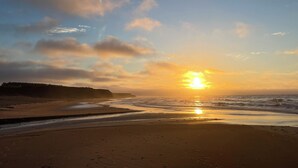 Une plage au coucher du soleil, avec des vagues douces et une côte lointaine.