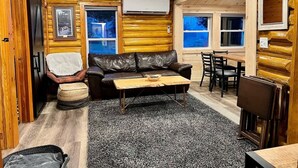 Een gezellig interieur van een chalet met een leren bank, een houten salontafel en een eethoek met stoelen.