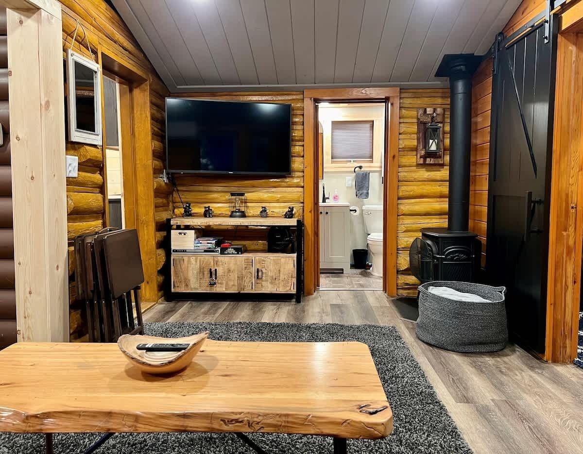 Ein gemütliches Blockhauss-Interieur mit einem Holztisch, einem Fernseher, einer Küchenzeile und einem Kamin.