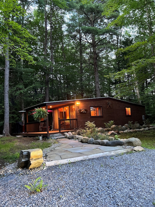 A rustic cabin with a wooden exterior, a porch, and a stone pathway leading to the entrance. - šSaratoga Track & Streamside Retreat š² - Relax, Hike, Shop & Dine! (Greenfield Center)