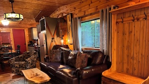 Een gezellig interieur van een chalet met een leren bank, een houten eettafel en een rustieke keukenhoek.