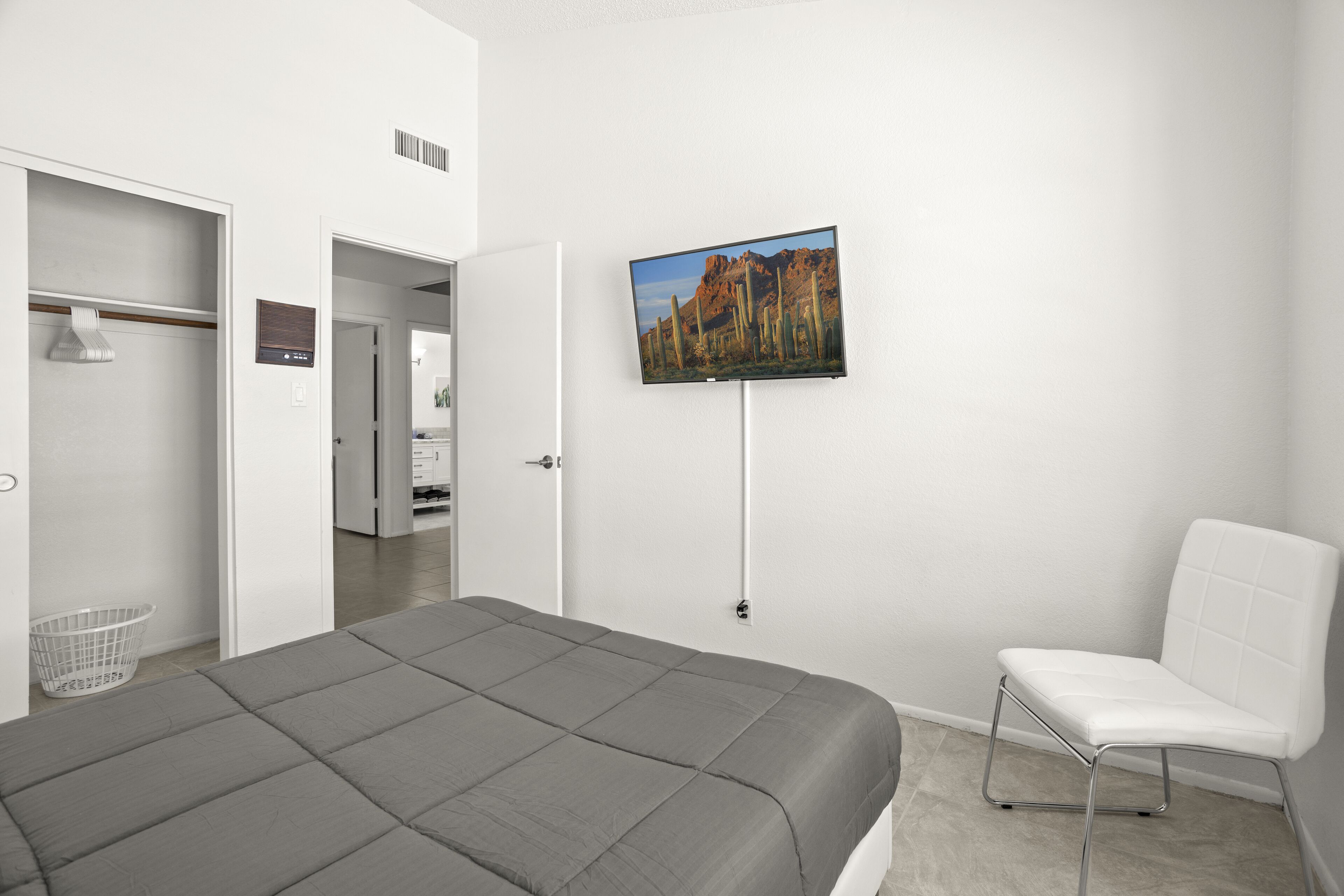 A bedroom with a bed, a white chair, a television on the wall, and a closet.
