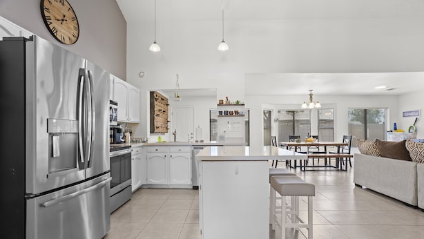 Una cucina moderna con elettrodomestici in acciaio inossidabile, un'isola centrale e un'area pranzo con tavolo e sedie bianche.