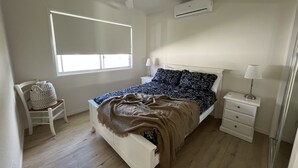 A bedroom with a bed, a chair, a nightstand, a lamp, a ceiling fan, and an air conditioning unit. - Hunter Valley guest house (Nulkaba)