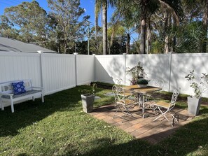 Ein Garten mit weißem Zaun, einer Bank, einem Tisch mit Stühlen und Topfpflanzen.