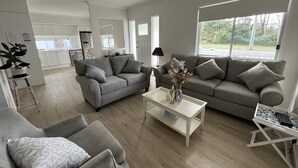 A modern living room with two grey sofas, a white coffee table, and a small side table. A ceiling fan is visible, and there is a window with a view of greenery outside. - Hunter Valley guest house (Nulkaba)