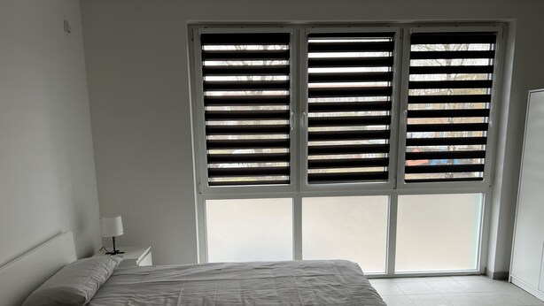 A bedroom with a bed, a nightstand, and a window with blinds. - Apart Rom Hannover Centrum (Hannover)