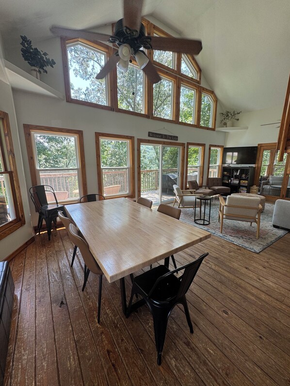 A spacious room with a large wooden table, multiple windows, a ceiling fan, and a sign reading 'Welcome to The Lake.'