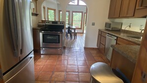 A kitchen with a stainless steel refrigerator, oven, and microwave. There is a trash can and a window with a view of the outdoors.
