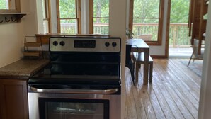 A kitchen with a stainless steel oven, wooden flooring, and large windows offering views of a deck and greenery.