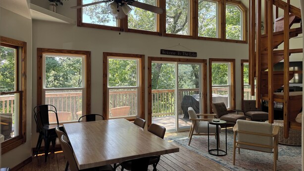 A spacious room with a large wooden table, multiple windows, a ceiling fan, and a staircase.