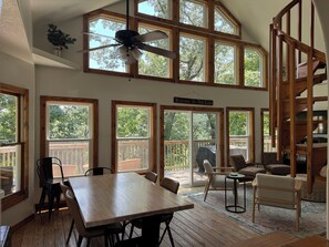 A spacious room with a large wooden table, multiple windows, a ceiling fan, and a staircase.