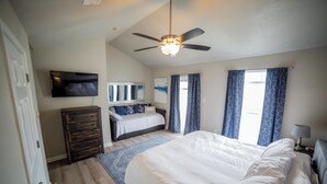 Une chambre Ă coucher avec un grand lit, un ventilateur de plafond, une tĂ©lĂ©vision, une commode et une fenĂȘtre avec des rideaux.