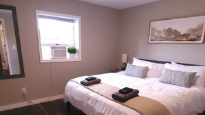 A bedroom with a large bed, a window with a view, and a painting on the wall. - Freshly updated apartment with ample outdoor space (Burdett)