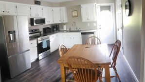 A modern kitchen with white cabinets, stainless steel appliances, a wooden dining table, and four chairs. - Freshly updated apartment with ample outdoor space (Burdett)