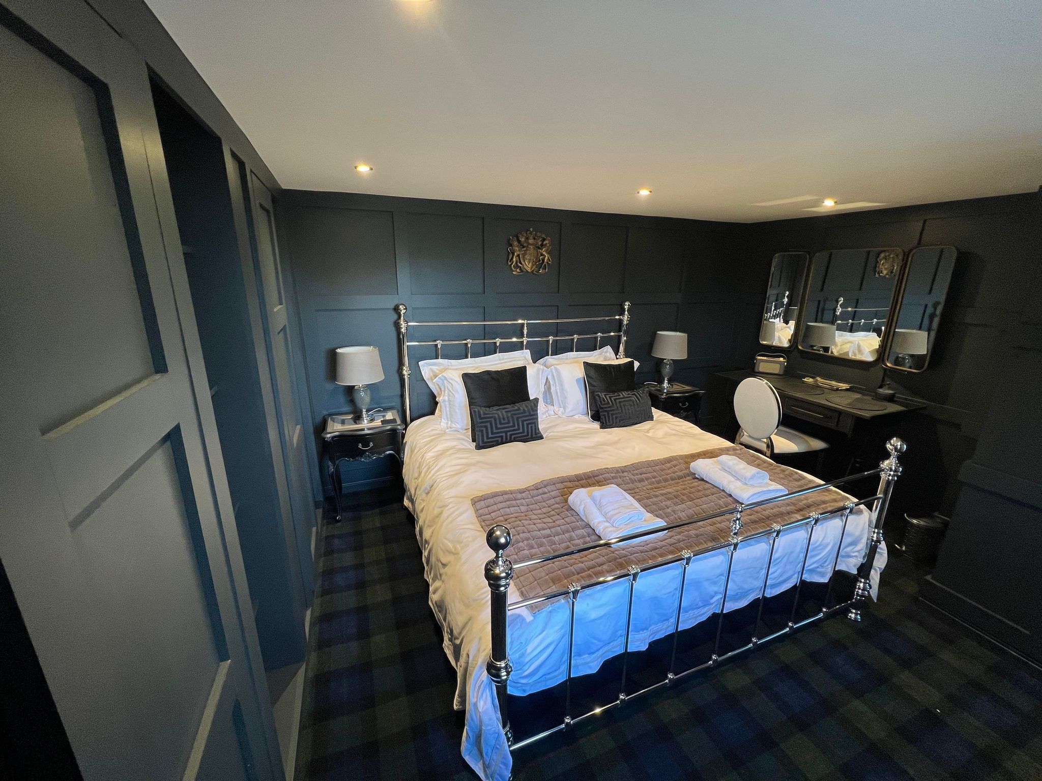 Une chambre d’hôtel moderne avec un grand lit, des tables de chevet avec des lampes, un bureau avec une chaise et un grand miroir.