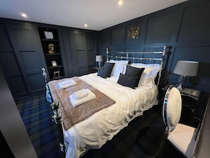 A modern bedroom with a large bed, bedside lamps, and a dark wood headboard.