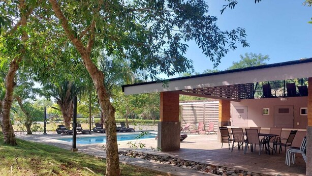 Uma área à beira da piscina com espreguiçadeiras, um alpendre coberto e vista para uma piscina.