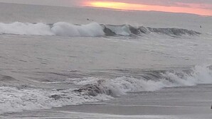 Uma praia com ondas e um pôr do sol ao fundo.