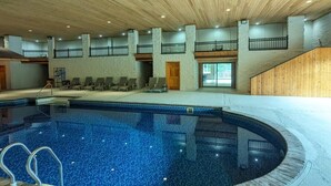Indendørs swimmingpool med træloft, flere niveauer med altaner og liggestole.