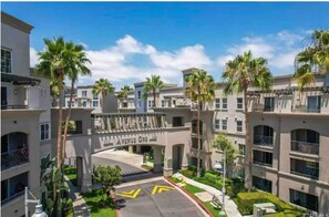 Welcome to Vanessa Avenue One, a residential building with a symmetrical facade and balconies on each floor, set amidst well-mainters landscaping with palm trees.