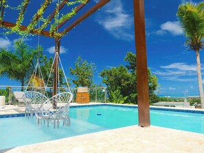 A pool area with a hanging chair, palm trees, and a clear blue sky.