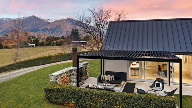 Une maison moderne dotée d’une cheminée en pierre, d’un espace salon extérieur et offrant une vue sur les montagnes.