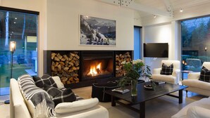 Un salon moderne avec une cheminée, des canapés blancs, une table basse et une grande fenêtre donnant sur la forêt.