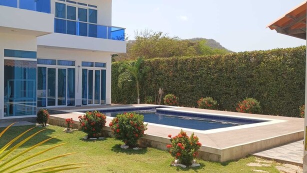 Ein modernes, zweistöckiges Haus mit Swimmingpool, umgeben von gepflegten Gärten und einer Hecke.