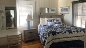 Una camera da letto con un letto, un comodino, una lampada, una sedia, una scrivania e una ventola a soffitto.