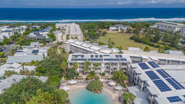 An aerial view of a resort with multiple buildings, a swimming pool, and a beach.