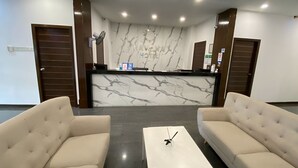 Uma área de recepção de hotel com parede de mármore, dois sofás, uma mesa de centro e um balcão de recepção.