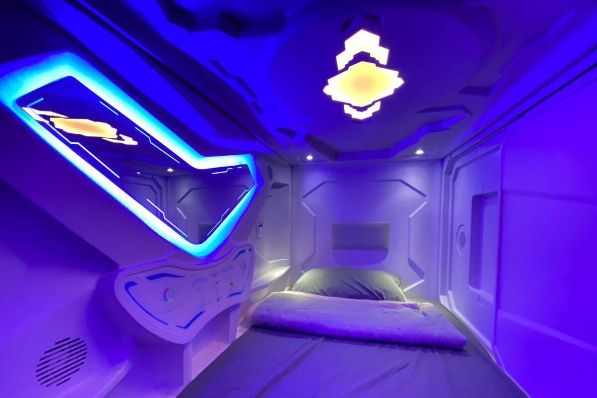 A futuristic room with a bed, a control panel, and a unique ceiling design.