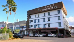 Edifício do Hotel Havona com uma placa, vários carros estacionados e uma palmeira em primeiro plano.