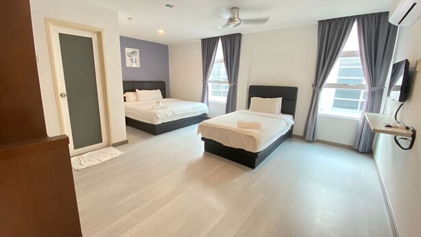 Quarto de hotel com duas camas, televisão de tela plana, ventilador de teto e janelas amplas com cortinas.