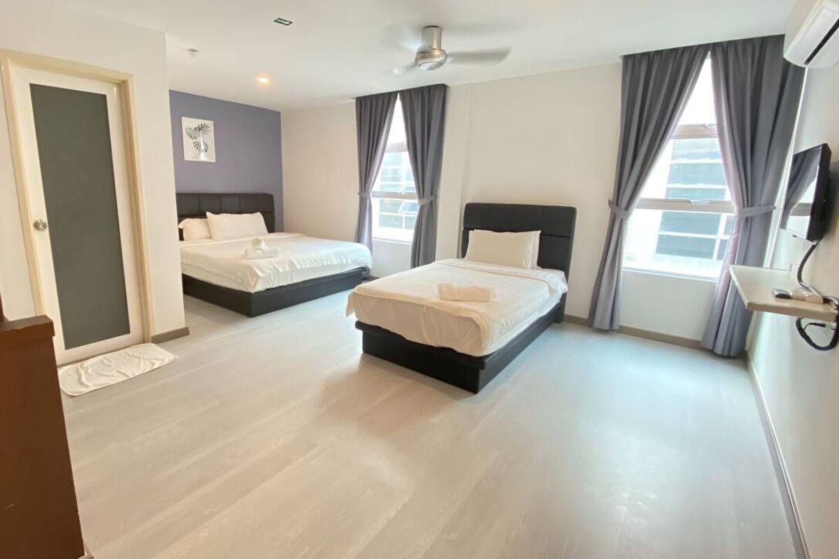 A hotel room with two beds, a flat-screen TV, a ceiling fan, and large windows with curtains.