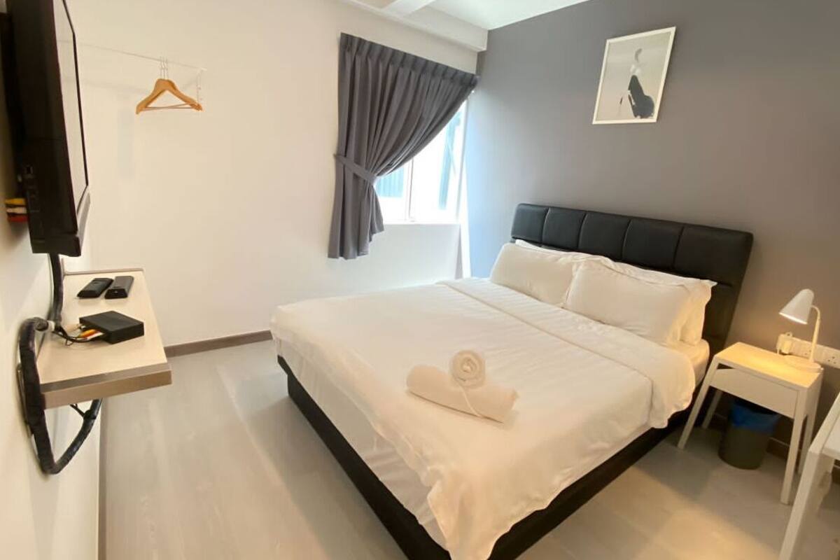 A modern hotel room with a large bed, bedside table, and a TV mounted on the wall.