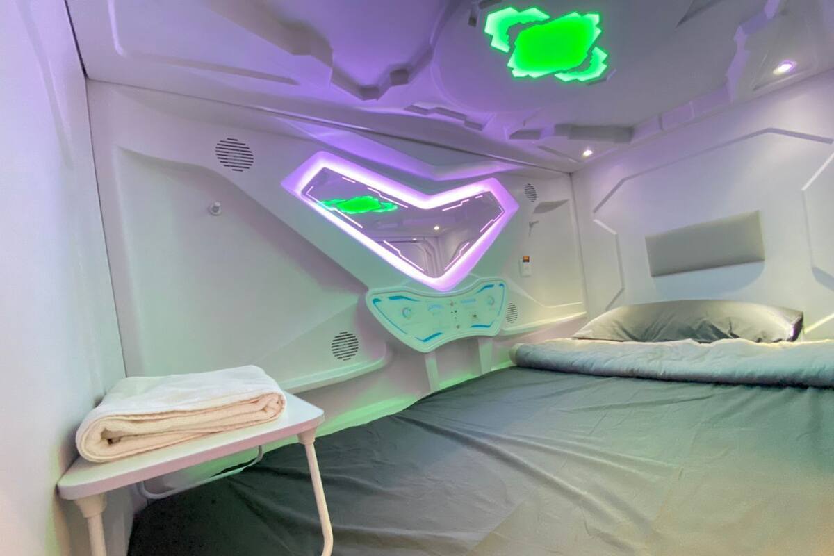 A modern bedroom with a bed, a bedside table with a towel, and a unique ceiling light fixture.