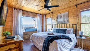 Een slaapkamer in een houten chalet met een bed, een plafondventilator en uitzicht op de natuur.