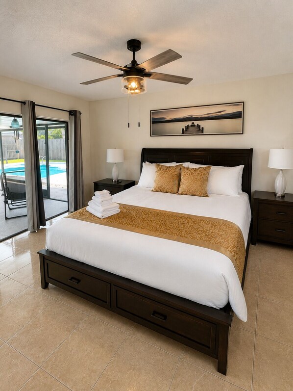 A hotel room with a bed, a ceiling fan, a painting, and a view of a pool.
